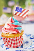 户外桌子上有红白蓝糖霜的纸杯蛋糕和美国国旗
