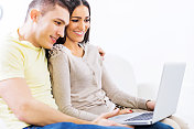 年轻夫妇在家里使用笔记本电脑。