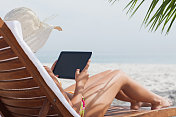 戴着帽子的女人在海滩上使用平板电脑