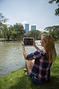 年轻女子在公园里使用数码平板电脑放松