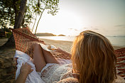 年轻女子躺在吊床上看海滩上的日落