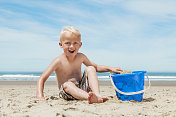 小男孩在沙滩上玩水桶。