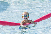小男孩在游泳池里戴着护目镜和面条