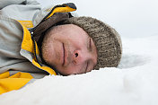 疲惫的男人穿着冬衣和帽子躺在雪地里