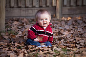 快乐的小男孩坐在秋叶中，面朝前方