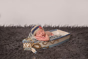 新生儿戴着航海针织帽睡在木制玩具船上