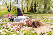 微笑的女人放松在草地在春日的大自然。