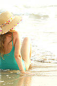 年轻女子戴着草帽坐在海滩上