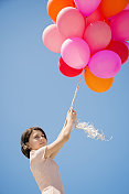 可爱的女孩拿着粉红色的气球捧着蓝色的天空。