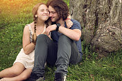 一对年轻夫妇坐在草地上拥抱在大自然中。