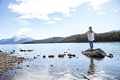 一个女人站在湖边的岩石上，张开双臂
