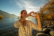 年轻女子在湖边做心形手指架