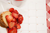 盘子里有新鲜的草莓水果。咖啡、甜点、日历。