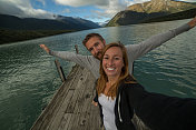 年轻夫妇在湖边码头上放松，拍自拍照