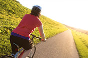 可爱成熟的女人骑着她的自行车在阳光下的小径