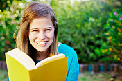 微笑的年轻读者的肖像在花园与打开的书
