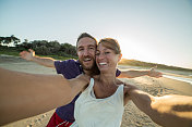 日落时分，一对年轻夫妇在海滩上自拍