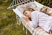 小女孩睡在吊床上，在后院休息。