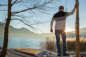 年轻人站在湖边的帆船上看日落