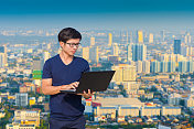 年轻的商人使用笔记本电脑和数字平板电脑的城市景观背景