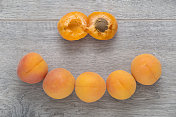 木桌上放着新鲜的杏子。五个完整的杏，一个切成两半。